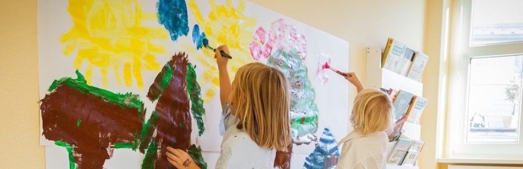 Kinder malen an großen Blättern an der Wand