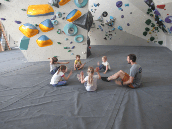 Kinder sitzen auf den Fallschutzmatten beim Bouldern